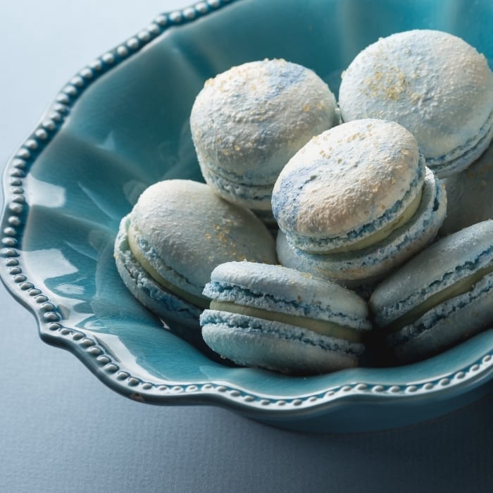 Blue bowl full of french macarons in blue color with cotton candy flavoring and a white chocolate ganache filling.