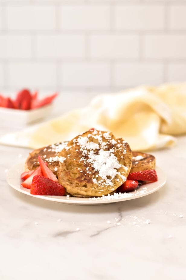 english muffin french toast on a plate with powered sugar and strawberries