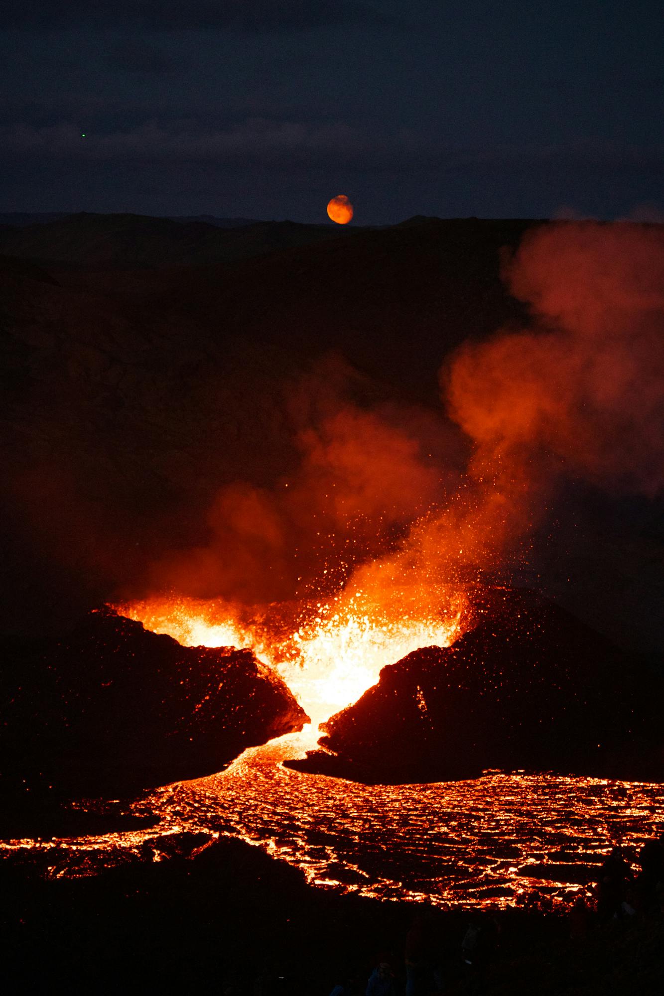 The moon rises over the lava flow at night