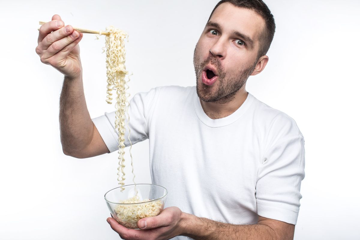 Man eating a bowl of noodles holding them high above his bowl