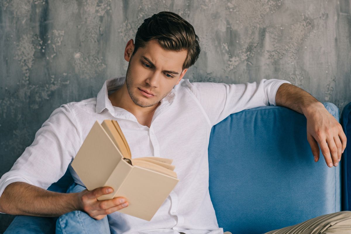 Man reading a book on a blue couch