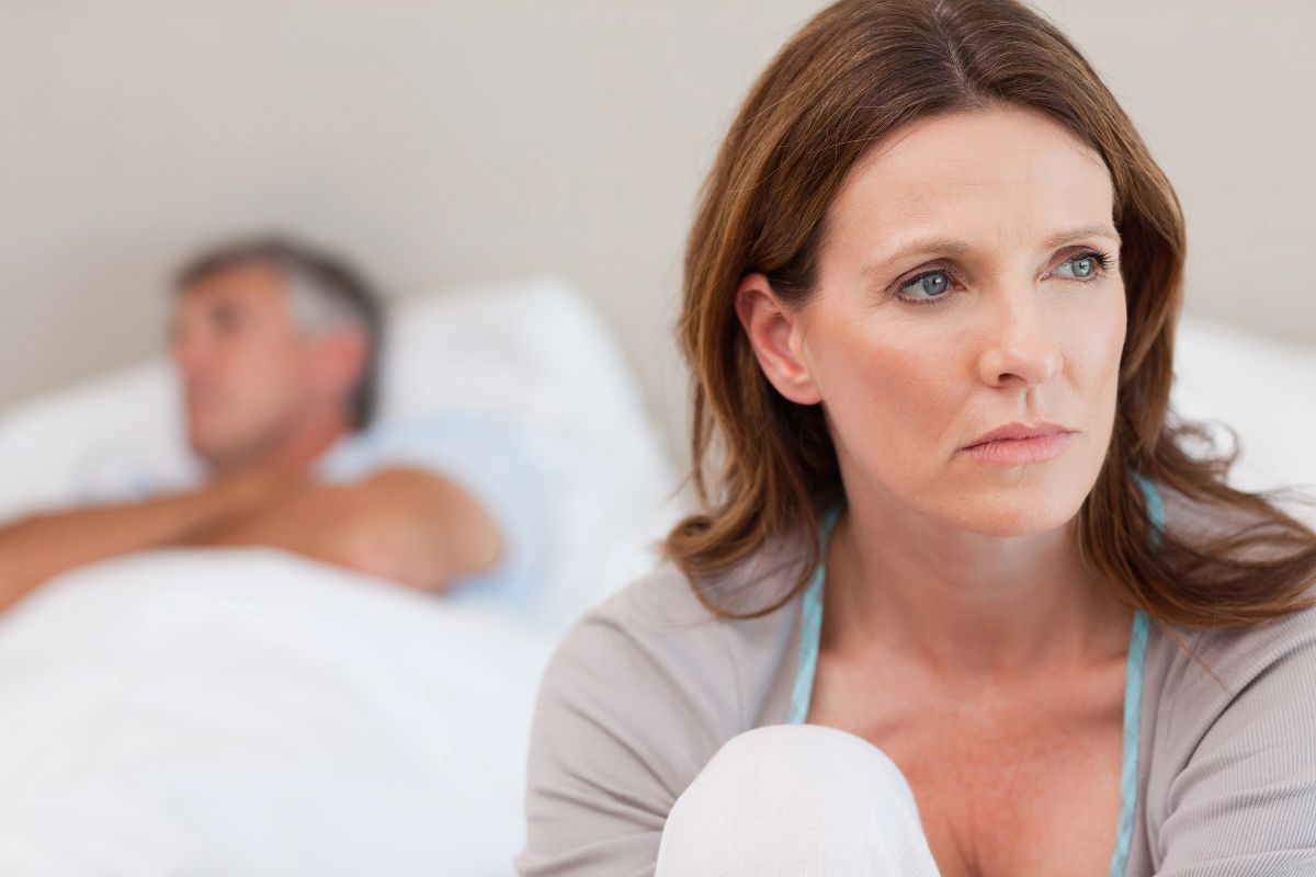 Woman looking sad with her husband in bed sleeping