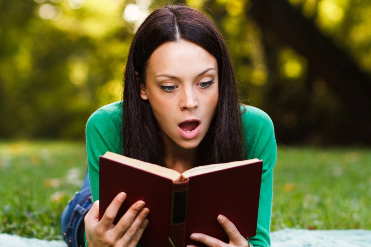 Woman reading a book shocked, reading outside.