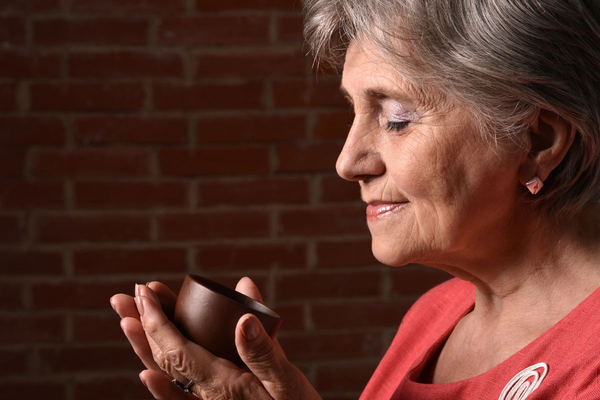 Older woman drinking coffee from a small brown bowl.