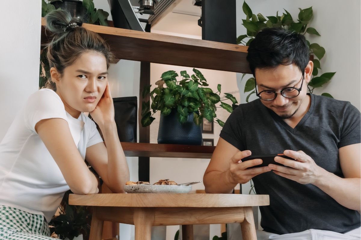 woman and man on a bad date, hes on his phone and she's annoyed