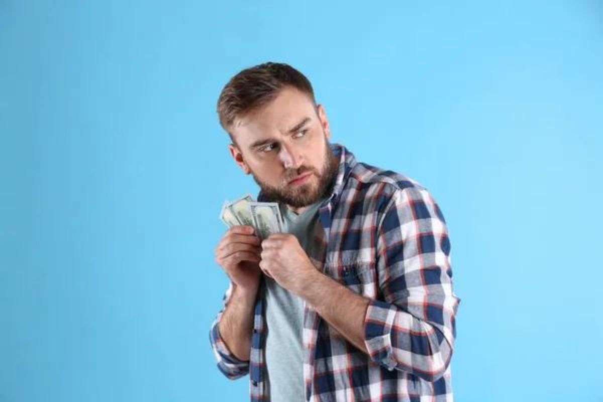 Man holding money close infront of a blue background