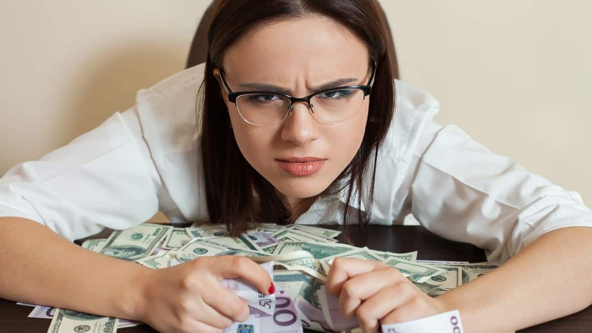 Woman holding money looking grumpy like someone will take it from her.
