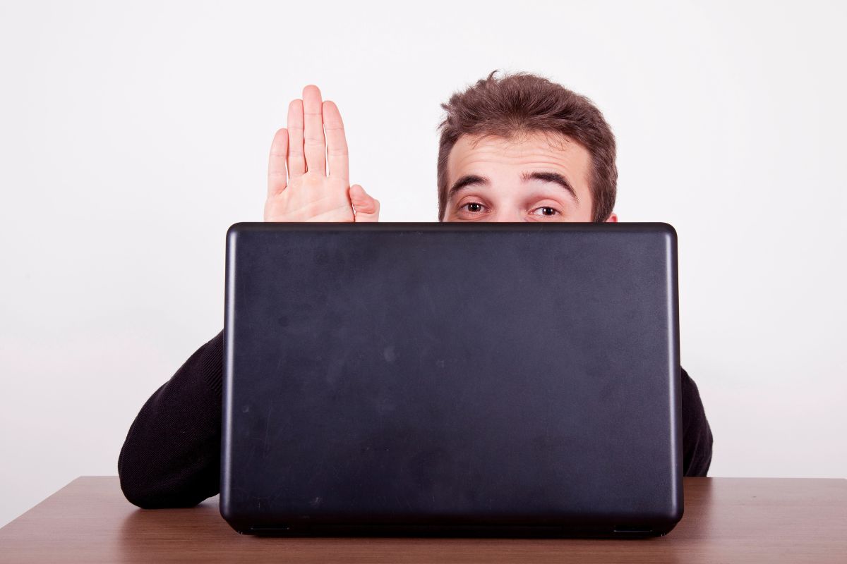 man hiding behind his laptop with his hand in the air