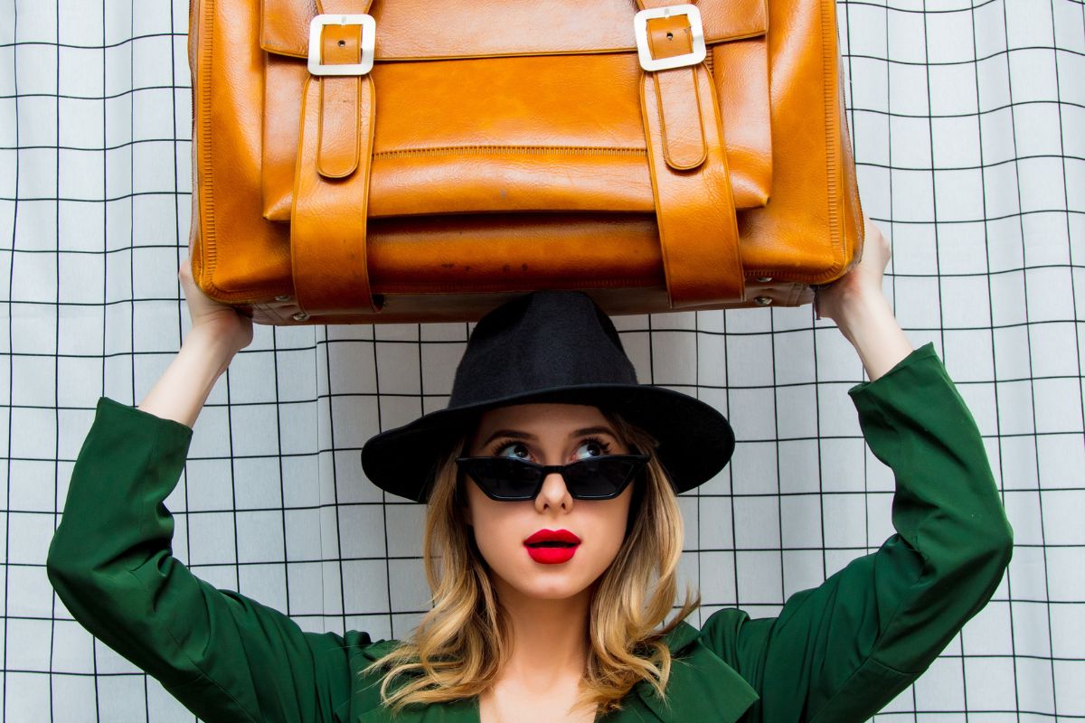 woman wearing a green trench coat and hat holding a suit case over her head