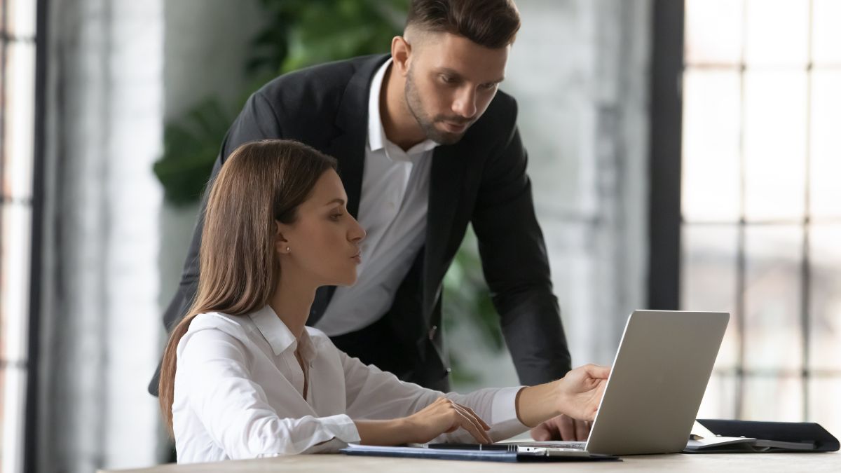 man helping woman on computer at work