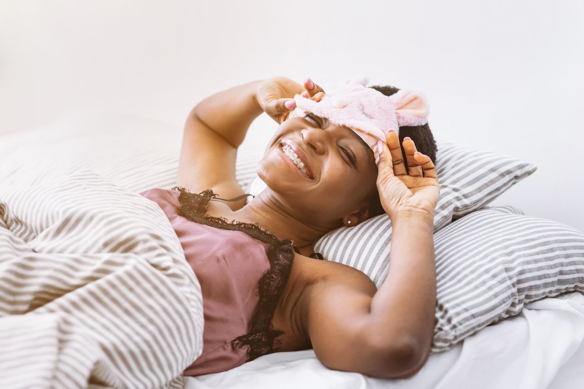 woman laying in bed smiling putting on her sleep mask