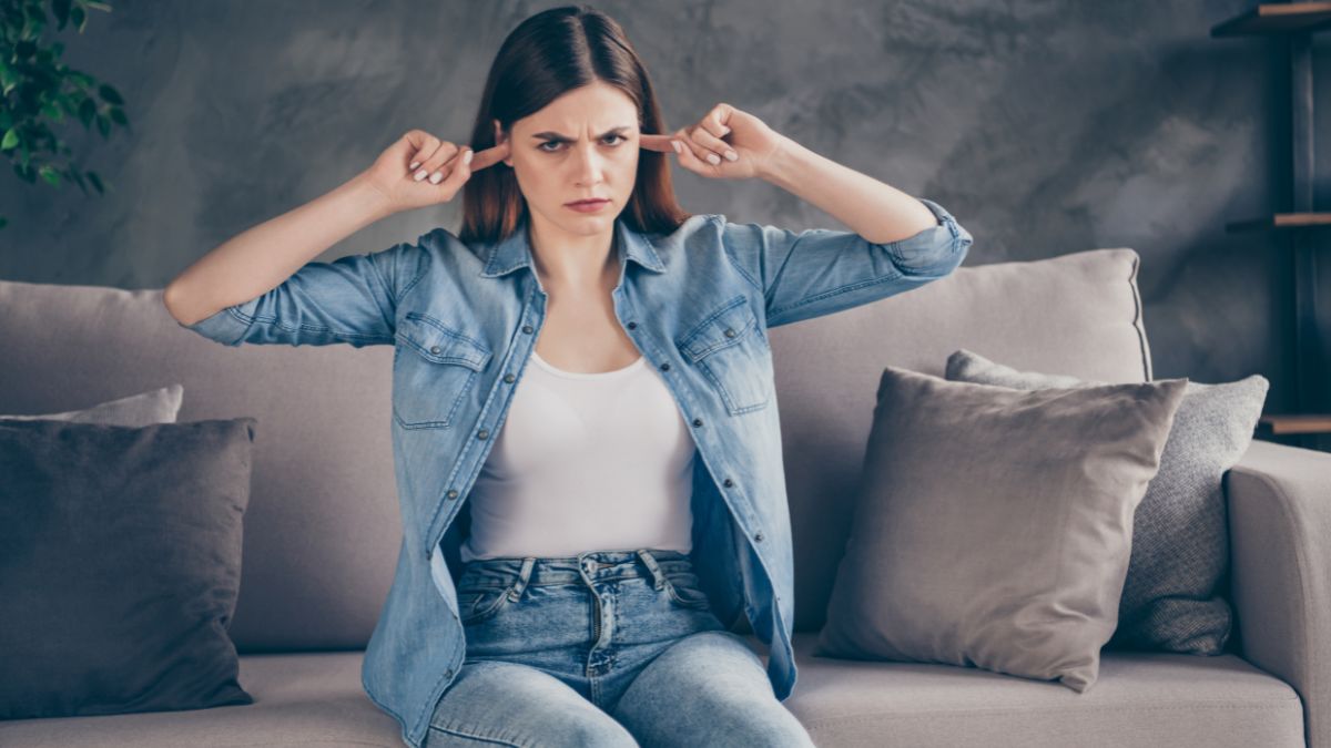 woman on couch with fingers in ears