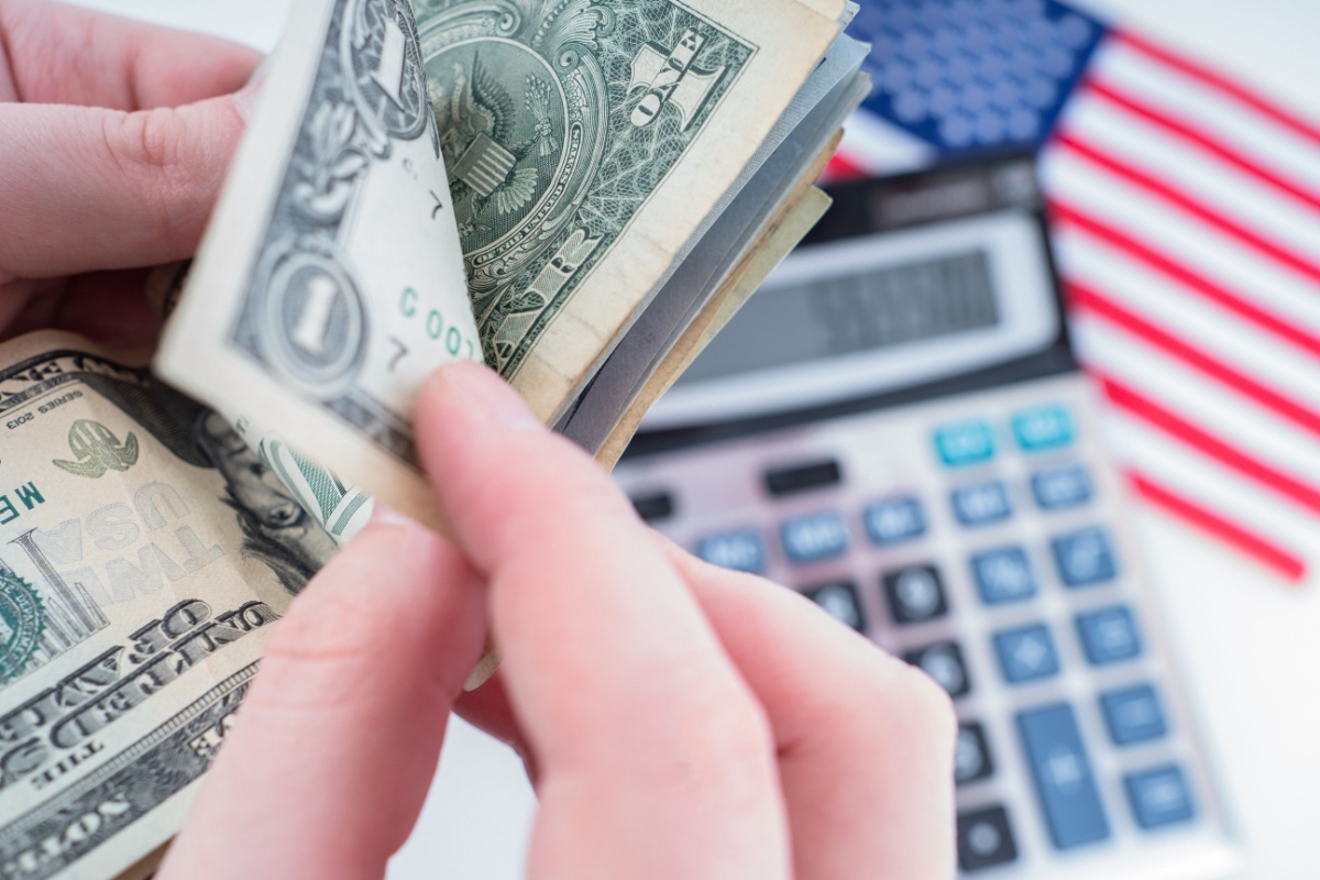 A person counts dollars against the background of the calculator and the us flag