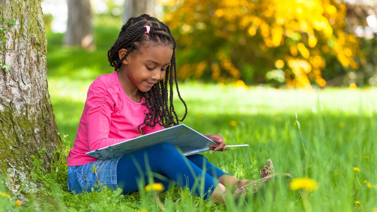 little girl reading by a tree