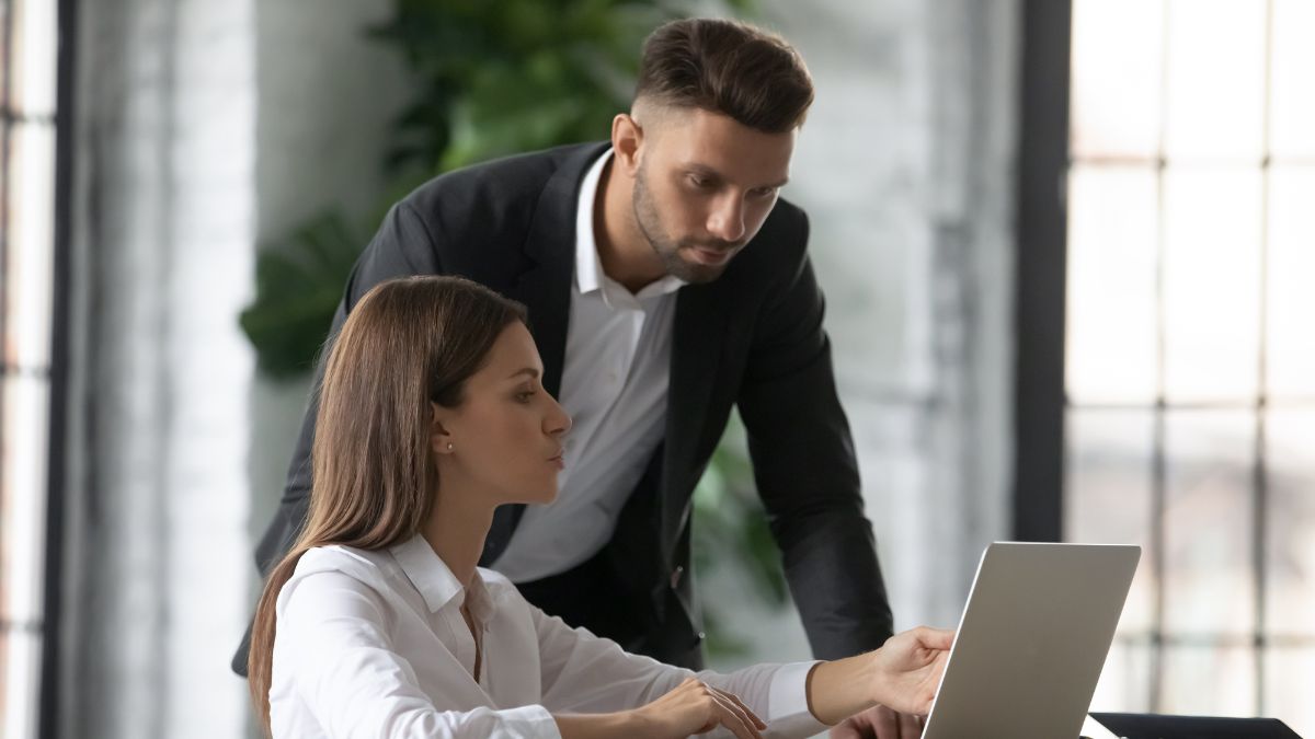 man helping woman on computer at work leaning