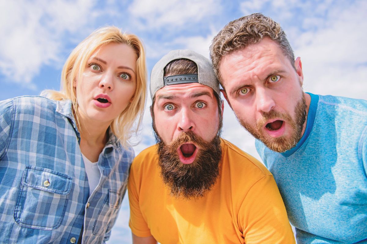 three people looking surprised, blue sky behind them.