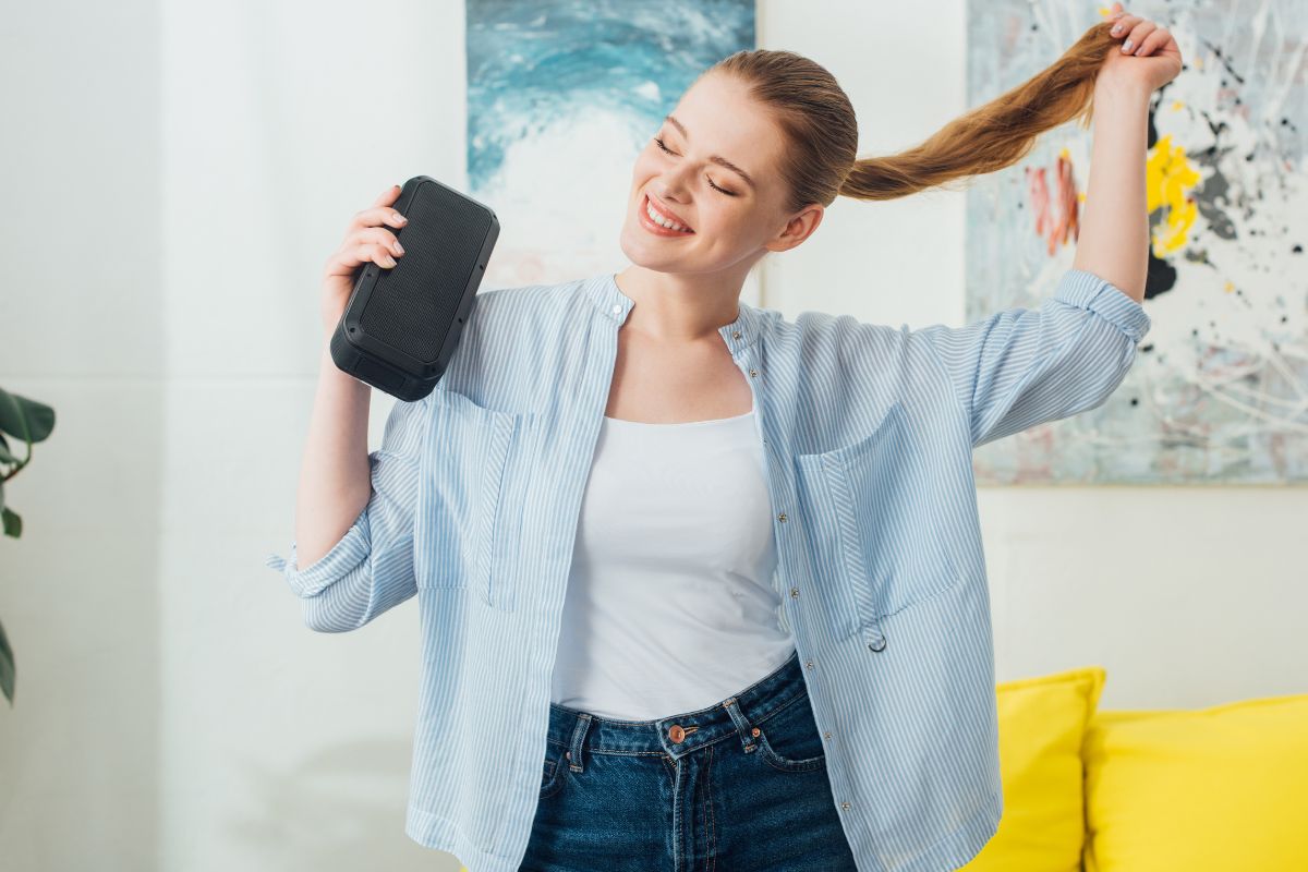 woman holding a speaker while dancing in her living room.