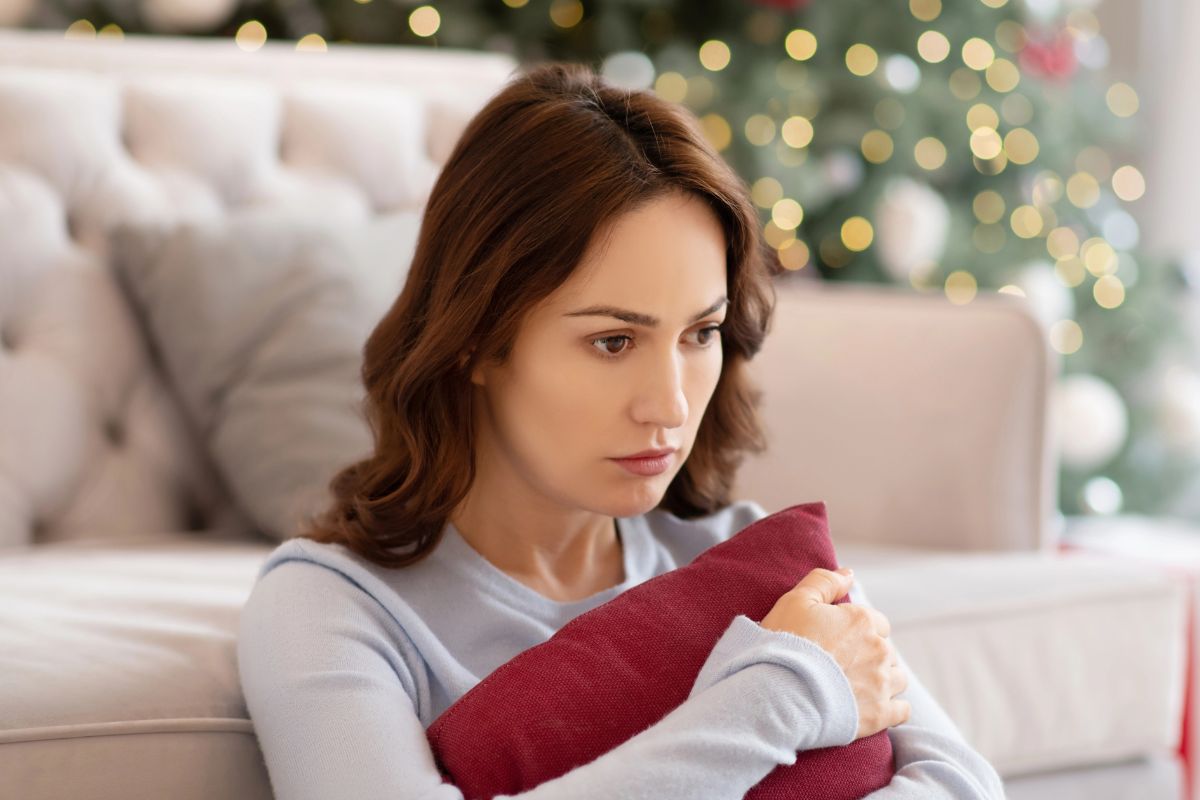 Sad woman holding a red pillow on the floor in the living room. christmas tree behind her.