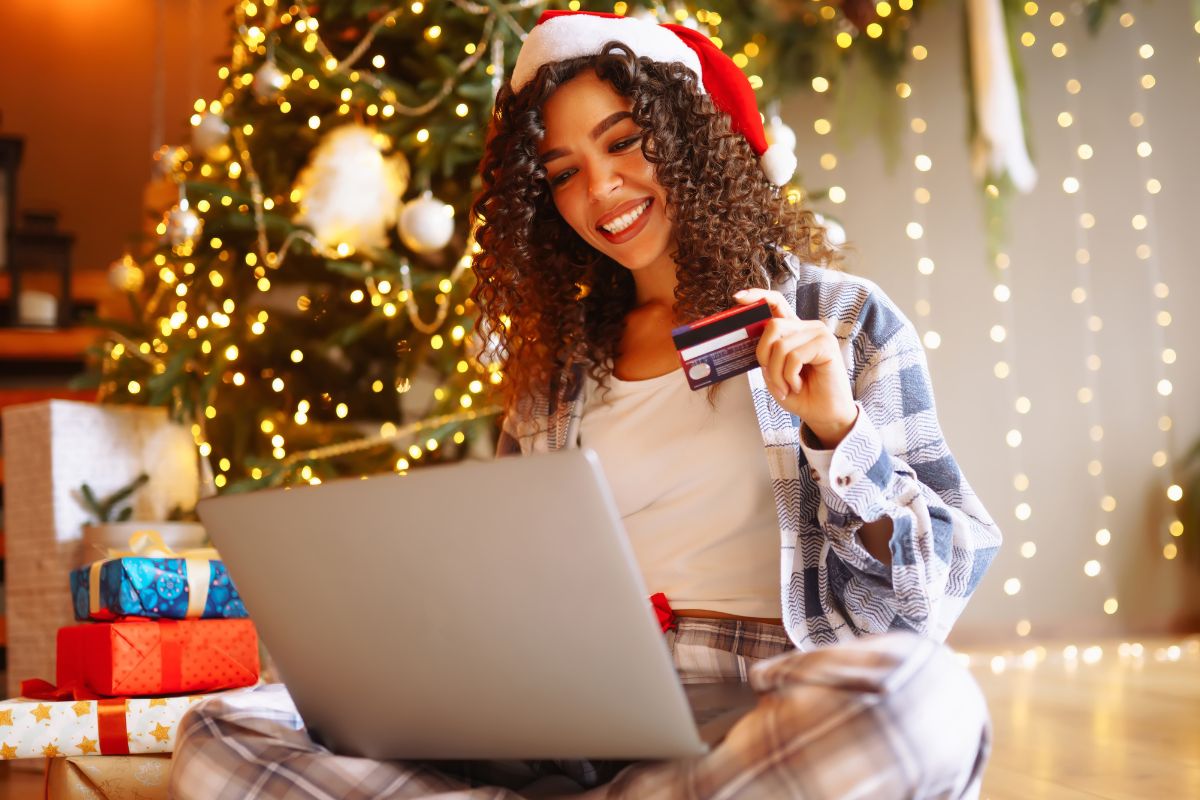 Woman holding a credit card infront of the laptop and a christmas tree behind her