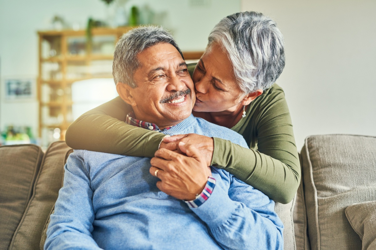 retired senior couple kiss on cheek on couch