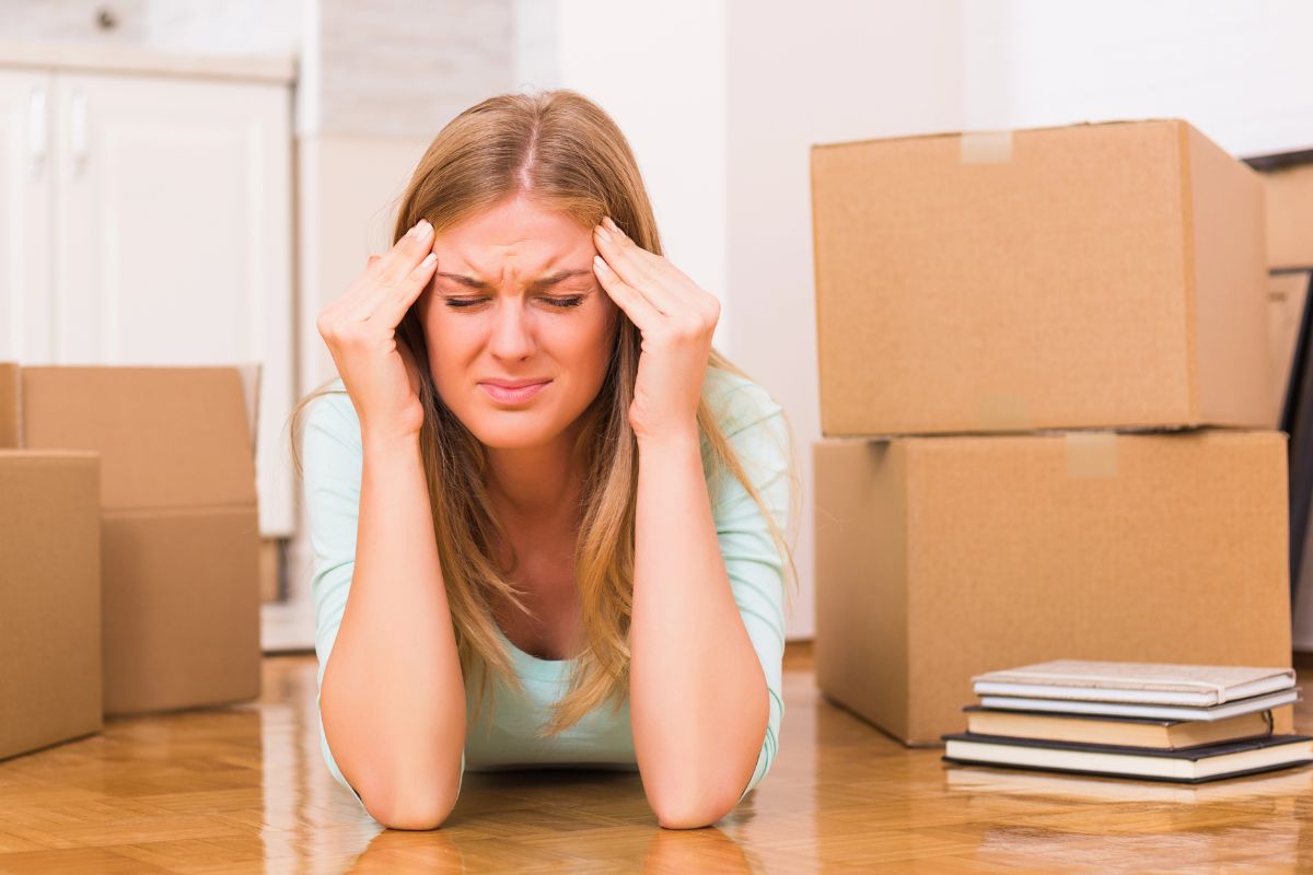 woman on the floor surrounded by moving boxes looking worried.