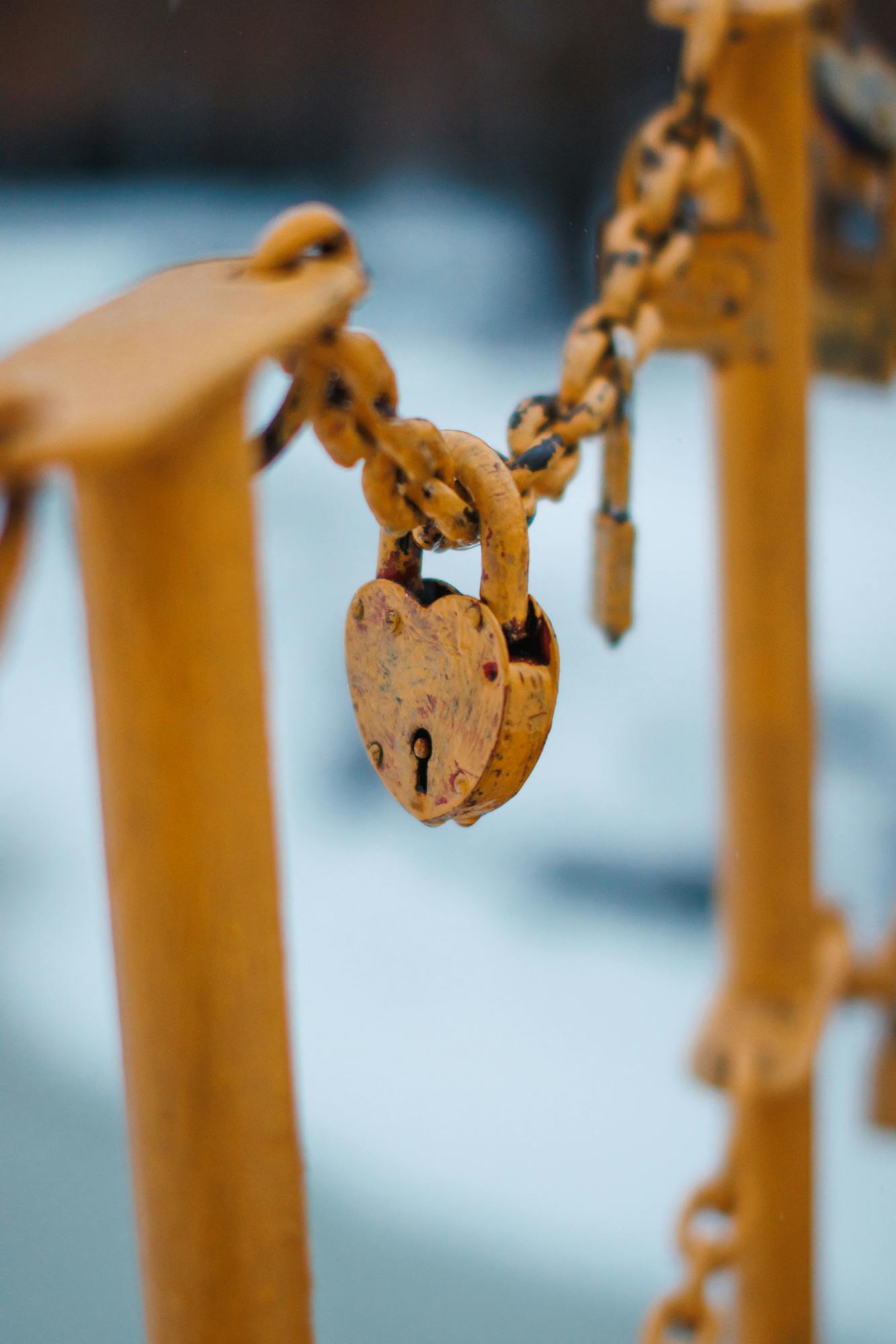 Close-up of a rusty heart-shaped padlock hanging from a yellow chain, symbolizing love and security outdoors.
