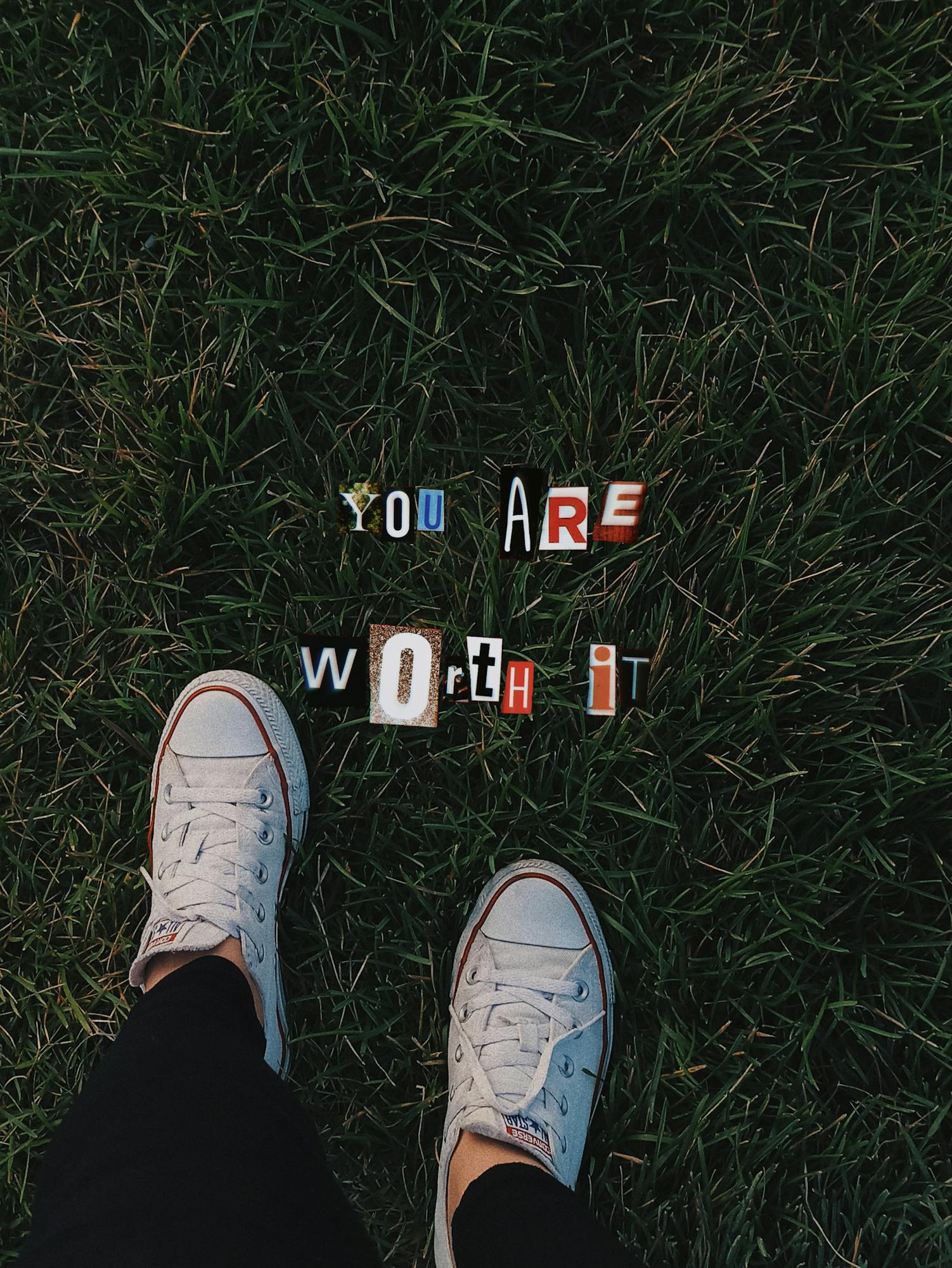 White sneakers on grass displaying a motivational message 'You are worth it'.