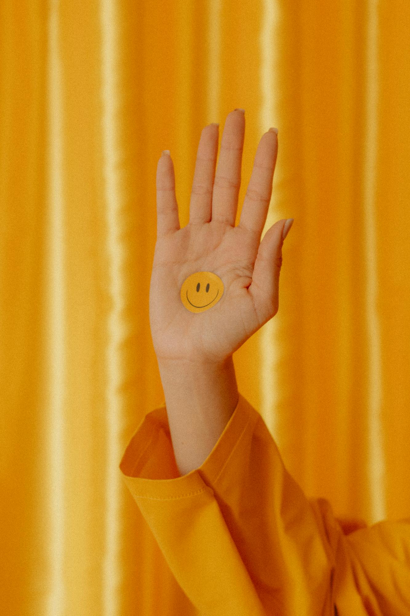 A hand featuring a smiley sticker stands out against a vibrant yellow backdrop, conveying positivity.