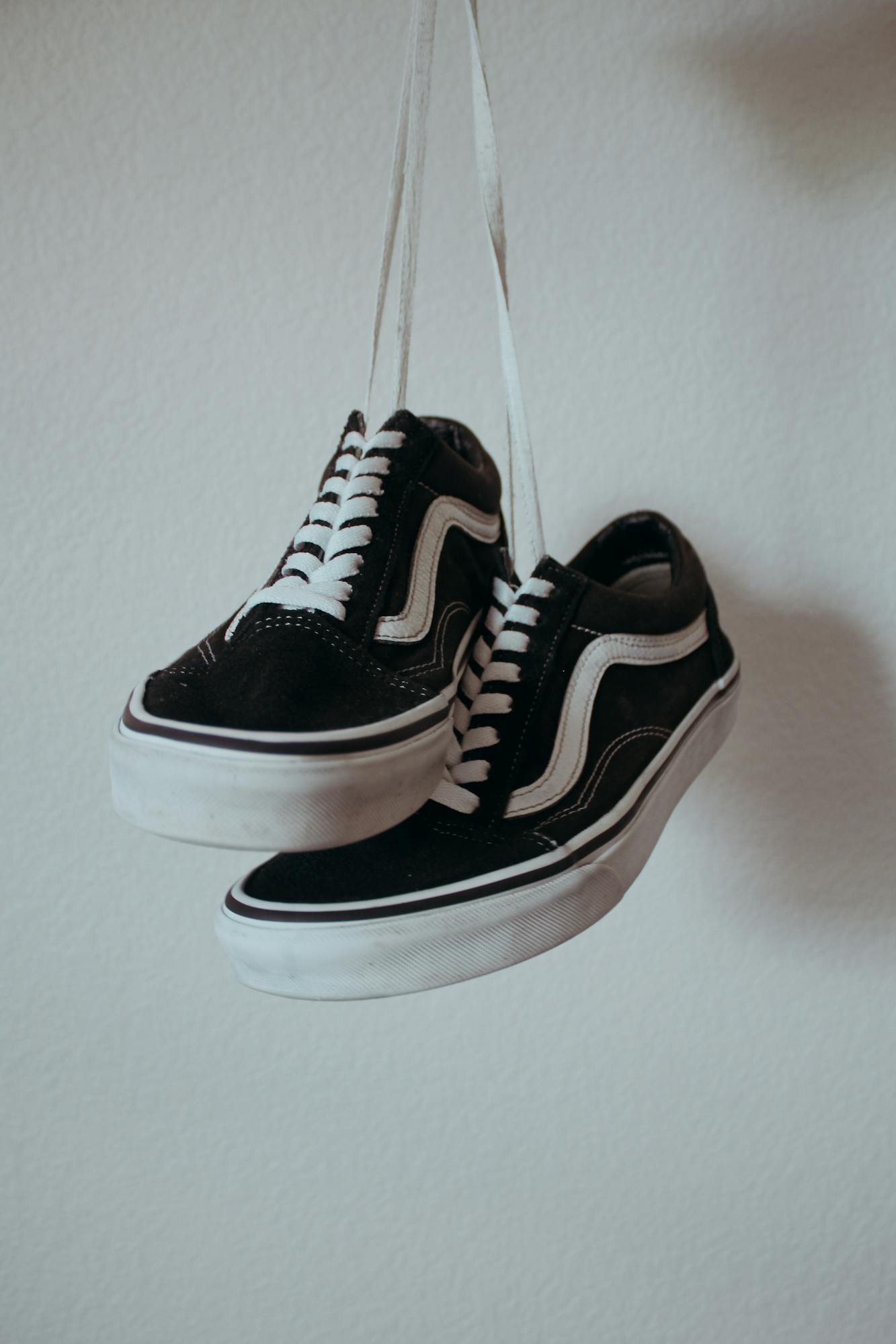 Black sneakers with white shoelaces hanging on a wall.