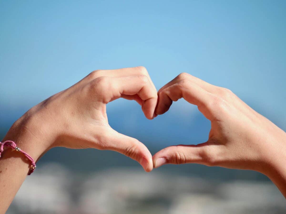 Close-up of hands forming a heart shape with clear blue sky background.
