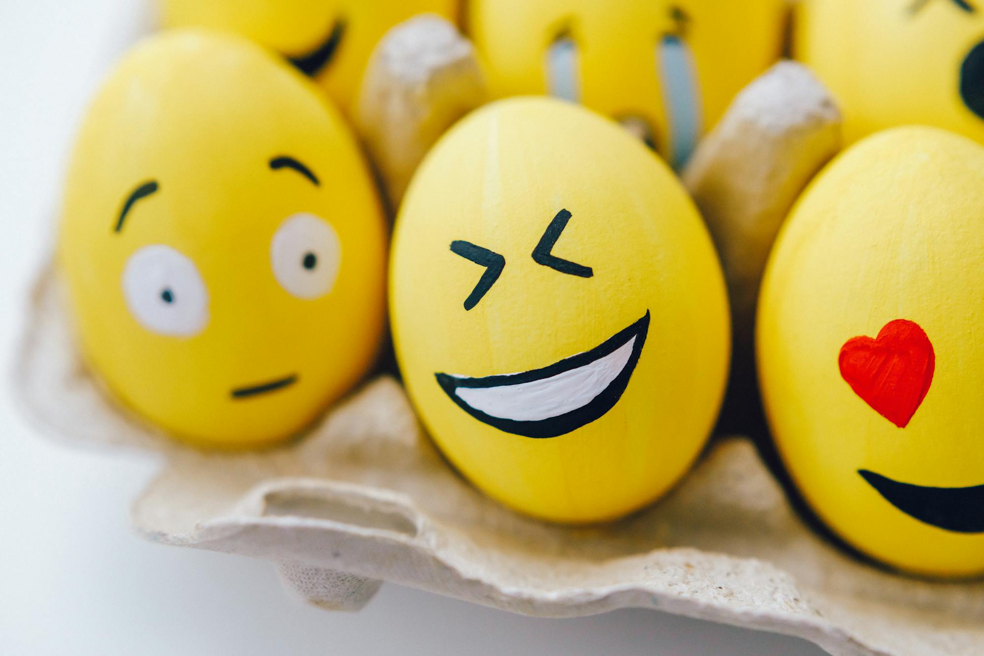 Colorful Easter eggs painted with emoji faces in an egg carton, perfect for holiday decoration.