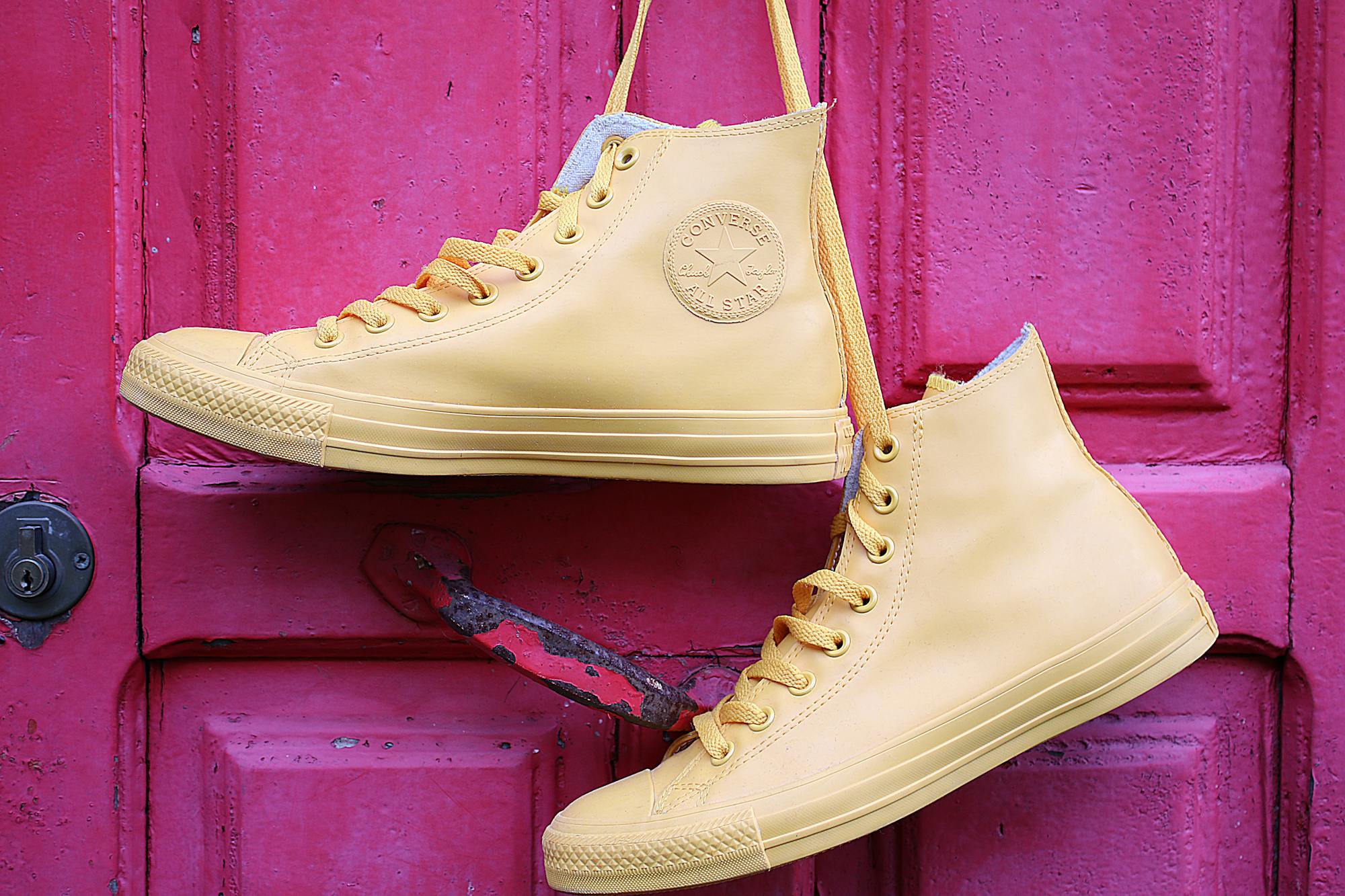 Stylish yellow high-top sneakers hanging on a vibrant pink painted door.