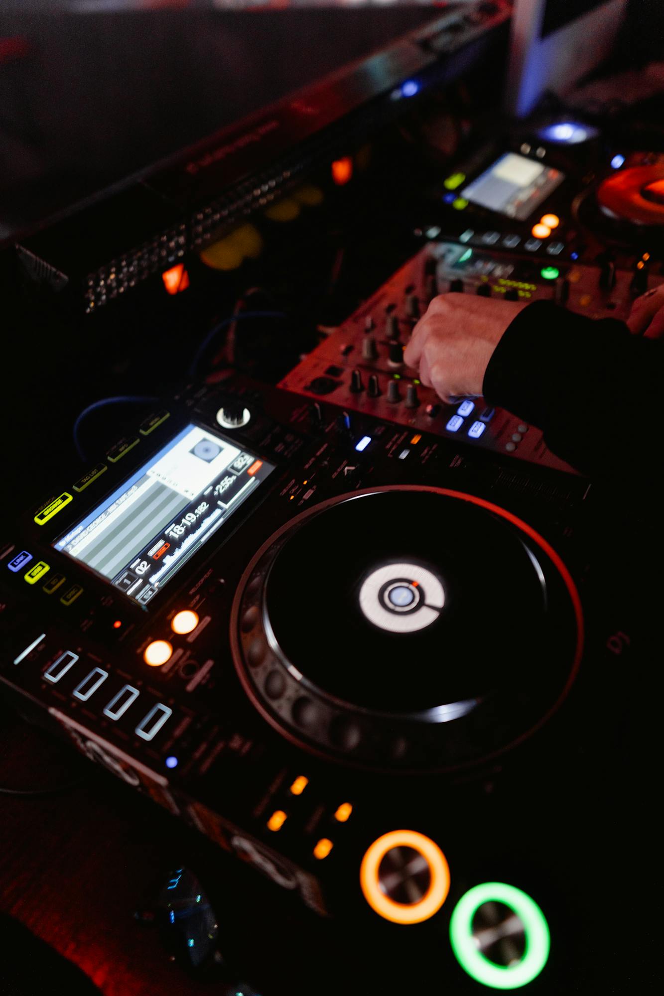 DJ hands skillfully mixing music on deck in vibrant nightclub setting.
