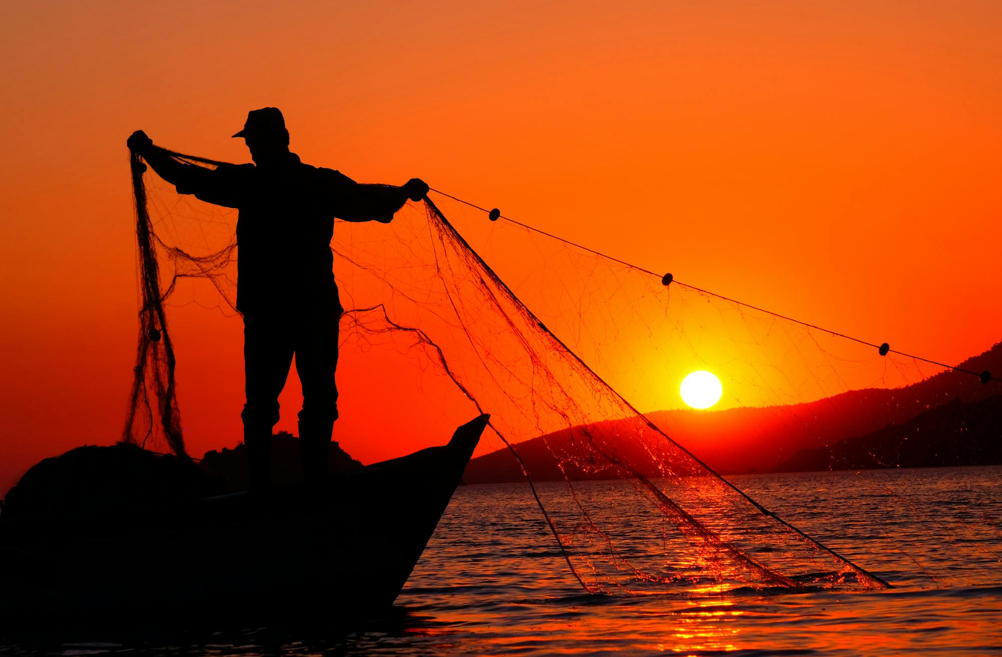 Silhouette of a fisherman holding a net against a vibrant sunset over the sea.