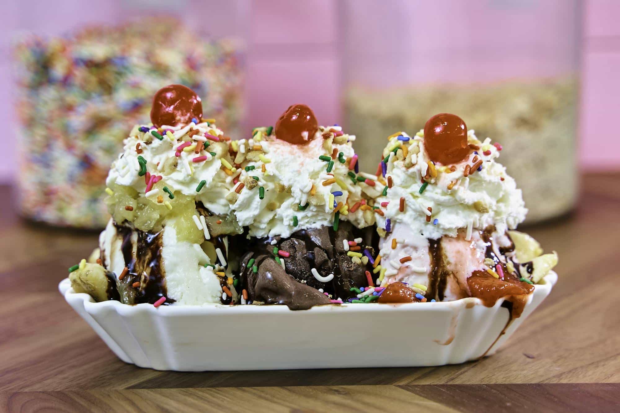 Colorful banana split ice cream sundae topped with whipped cream, cherries, and sprinkles.