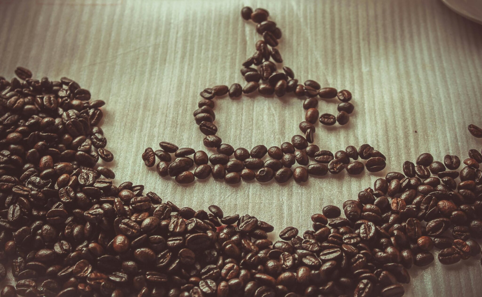 Creative arrangement of coffee beans forming a cup on a light wooden table.