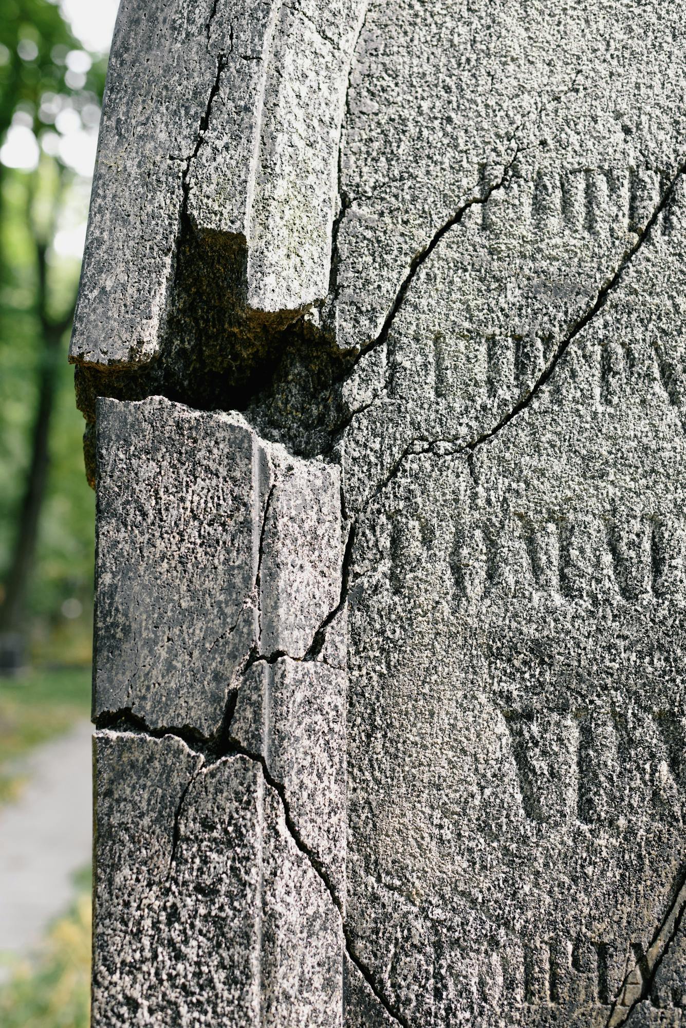 Close-up of a cracked tombstone showcasing detailed stone texture in an outdoor cemetery.