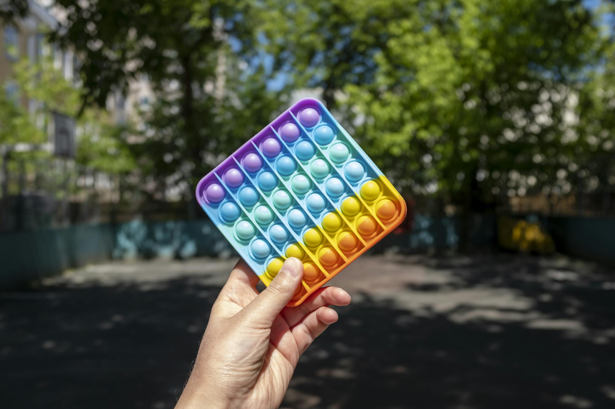 Vibrant rainbow Pop It toy held in hand with blurred outdoor background.