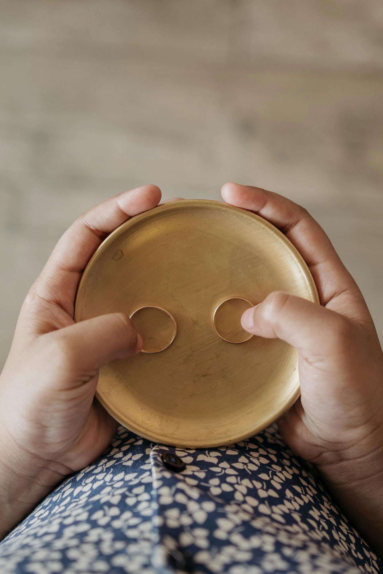 A close-up of hands holding a golden plate with wedding rings, top view.