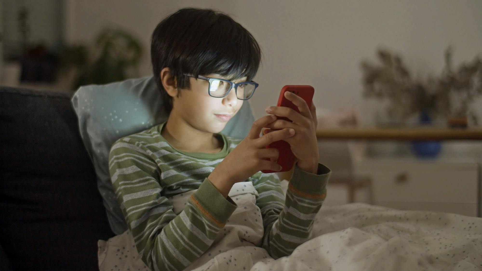 Young child using a smartphone alone in a bedroom, representing the kinds of devices and apps where groups like 764 target kids.