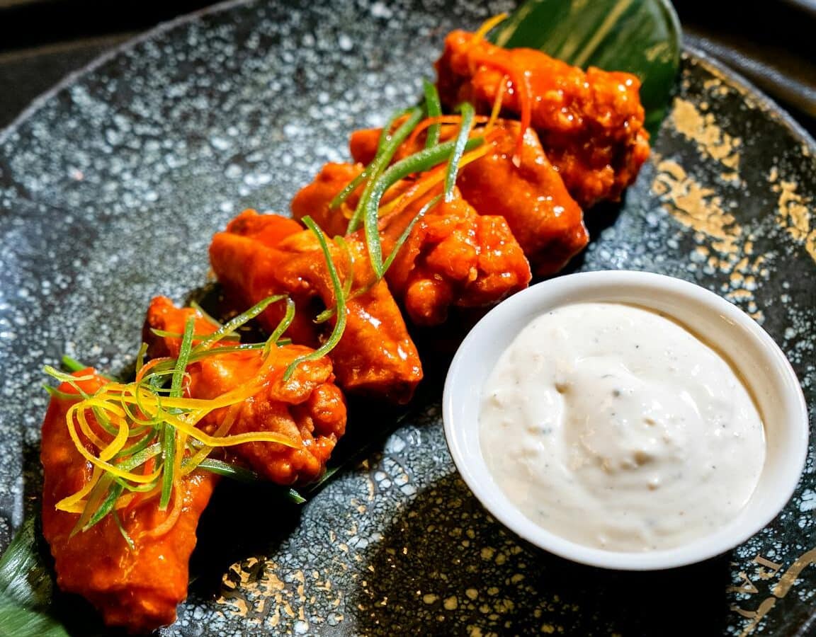 Crispy buffalo wings with creamy dip served on a stylish plate.