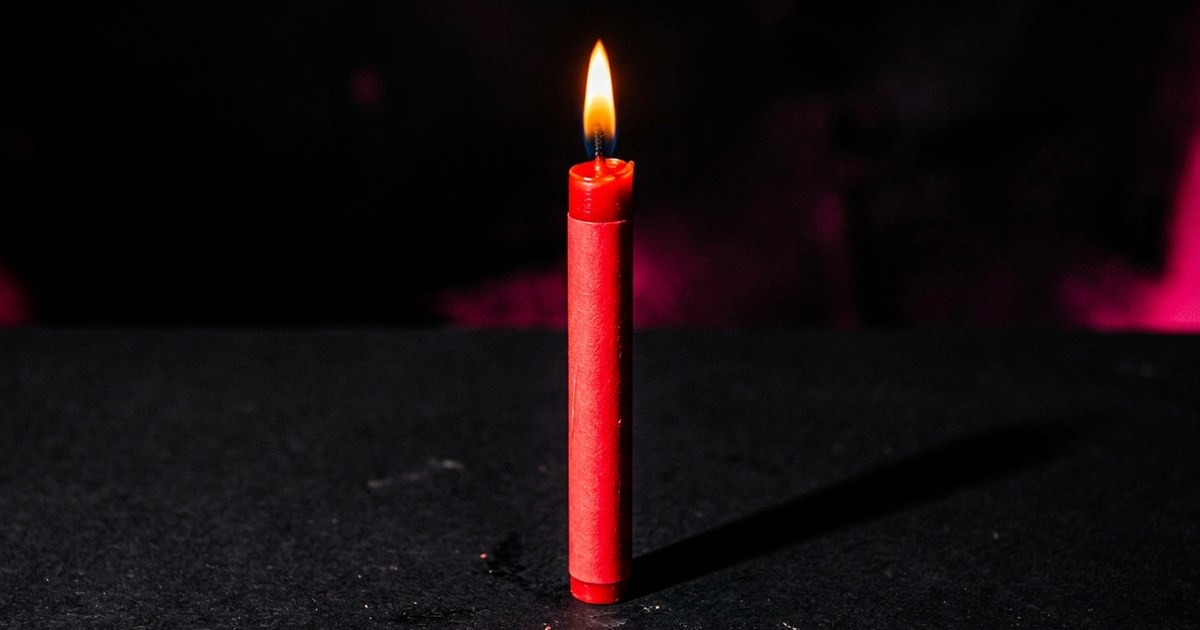 A red candle burns steadily in the dark — showing controlled slow burn